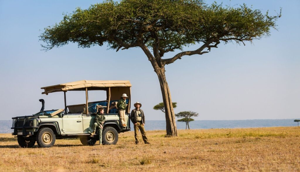 Volunteers standing by safari vehicle under tree in Africa