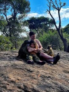 Family volunteers sitting with a baboon on a rock during a baboon bush walk